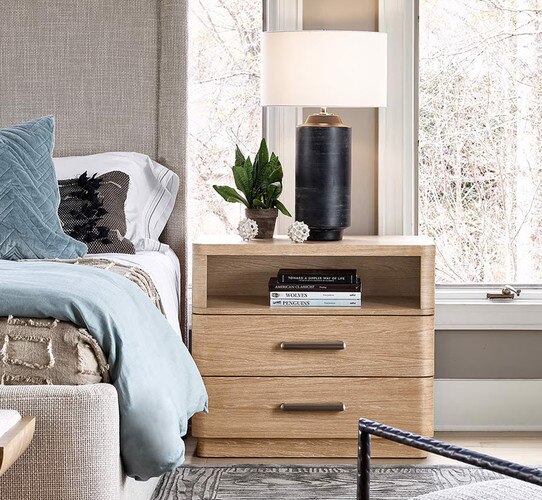 Wood nightstand holding a black lamp next to a bed