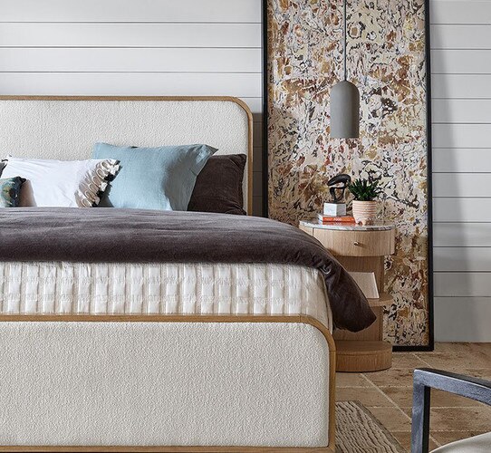 Wood and fabric bed frame beside a wood side table and large vertical abstract painting