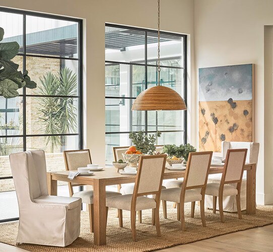 Dining table in front of two ceiling length windows and a large woven pendant light