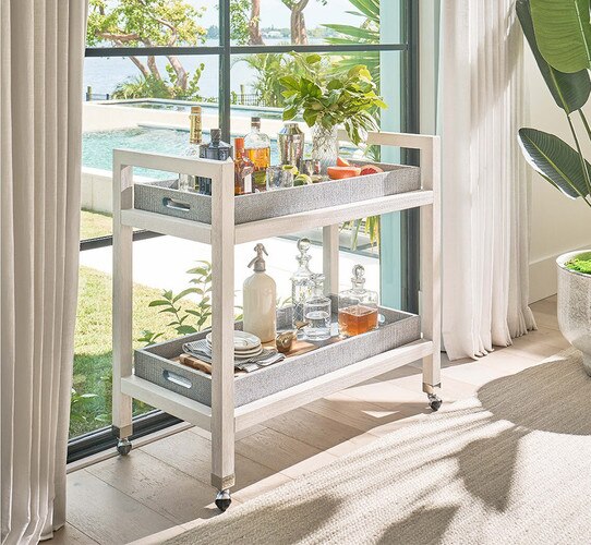 Bar cart with gray trays holding liquor bottles fruit and vases