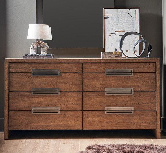 Wood dresser with inlaid metal handles holding a white lamp, books, and dÃ©cor