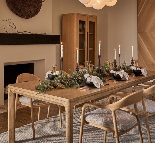 Long wooden dining table holding garland candles and place settings