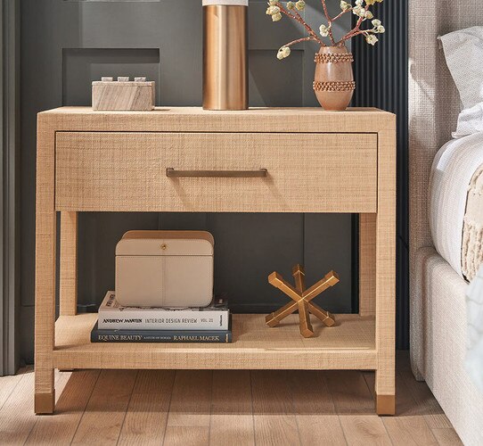 Tan nightstand with an open lower shelf holding books and a brass sculpture