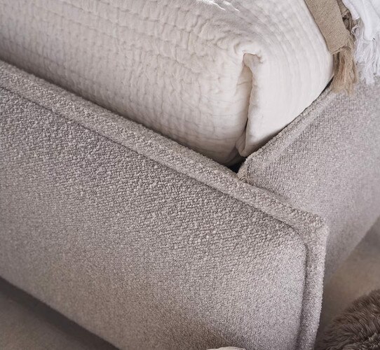 The corner of a gray linen bed frame