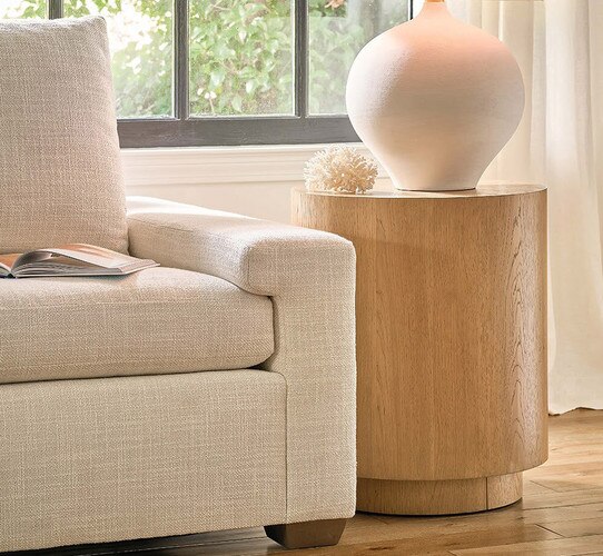 Drum wood side table holding a white lamp beside a white sofa