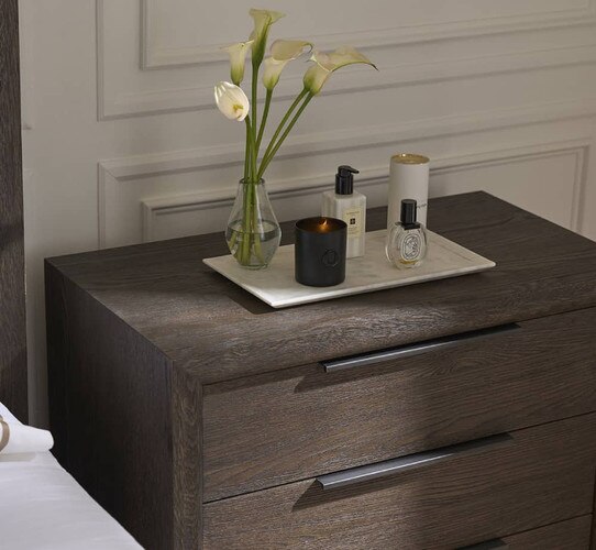 Wood nightstand holding small tray of facecare products and a vase of lilies