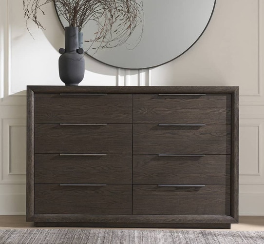 Dark wood dresser with eight drawers holding a vase under a circular mirror
