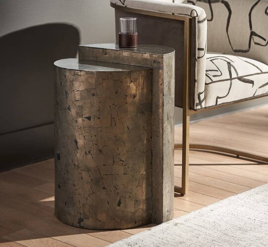 Cylindrical metal side table beside a modern white fabric chair