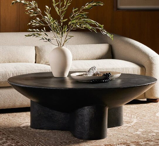 Black circular coffee table holding a white ceramic vase in front of a white sofa