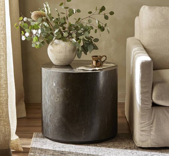 Circular black marble side table holding a white vase with eucalyptus