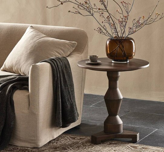 Dark wood side table holding opace vase with sticks in it