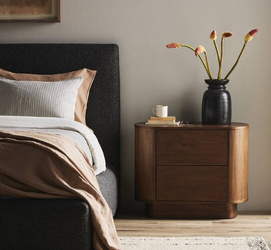 Oval nightstand holding a black vase and a stack of books
