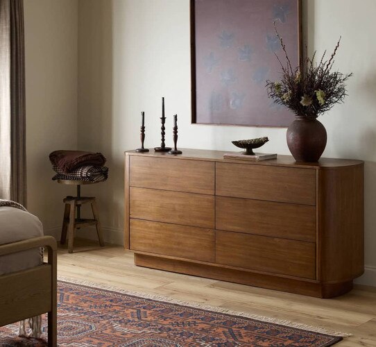 Oval wood dresser under a maroon painting of flowers