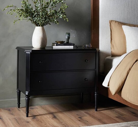 Traditional black wood nightstand holding a white ceramic vase with greenery