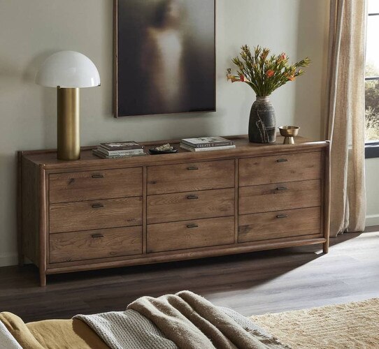 Nine drawer wood dresser holding books and a brass and white lamp
