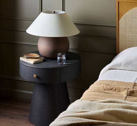 Circular nightstand with a flared base holding a table lamp