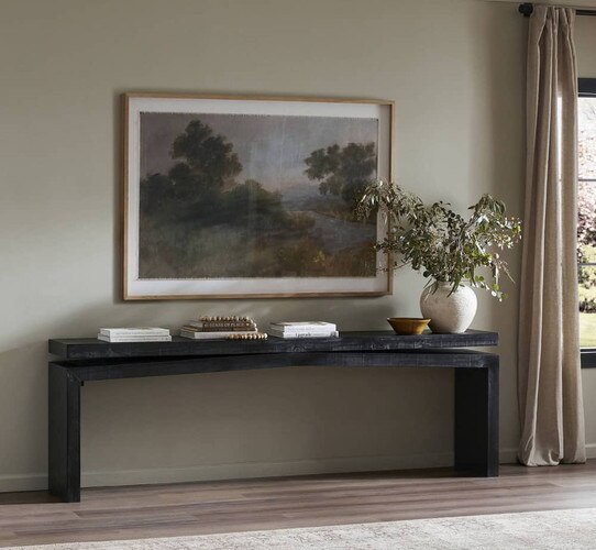 Black wood console table below a landscape painting