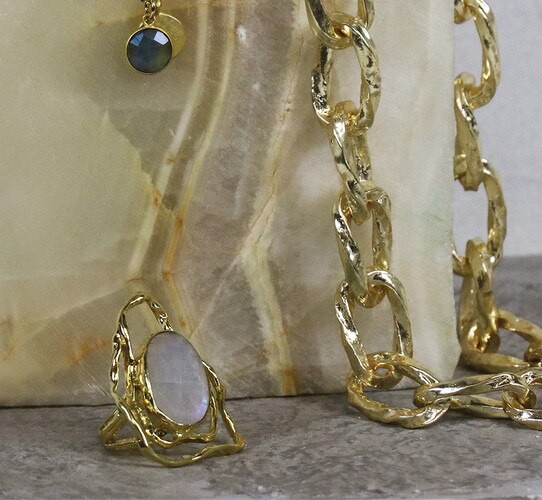 Gold chain necklace draped over a stone with a gold ring placed in front of it