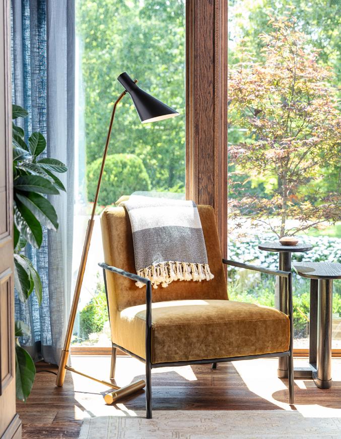 brown leather chair and task floor lamp next to two tall windows that show greenery