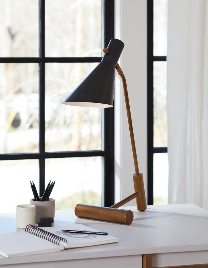gold and black task lamp on white desk next to a notebook