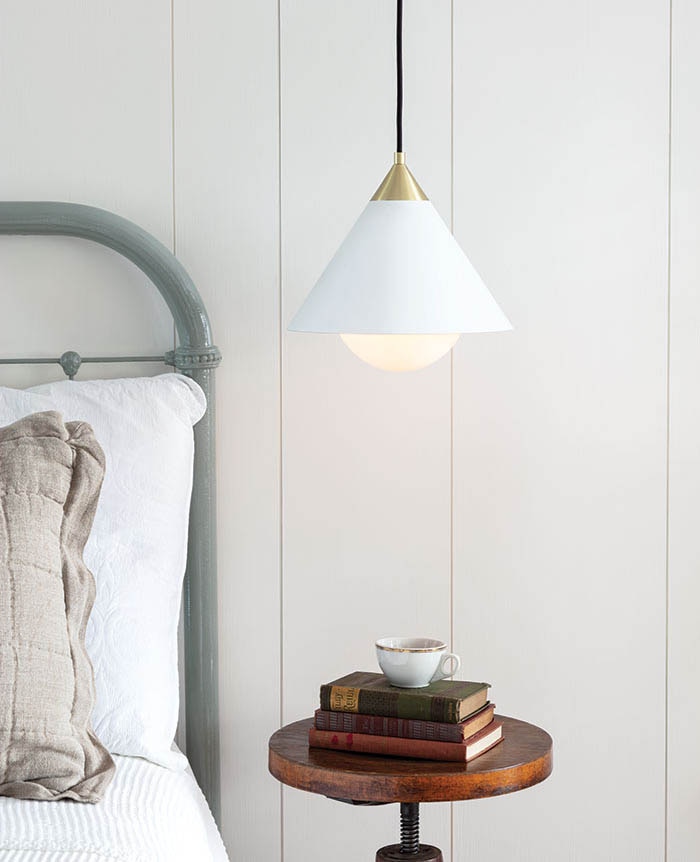 Cozy bedroom side table stacked with books and a tea cup, with a white and natural brass hanging ceiling pendant