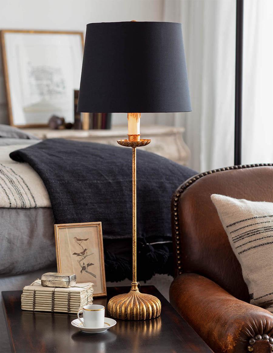 Cozy bedroom with a leather chair, and side table with a photo, a cup of espresso, and a golden antiqued gold lamp with a black shade