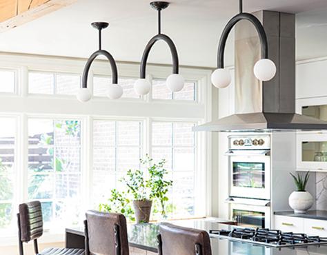 Sunlit kitchen with leather chairs and three modern curved black ceiling pendants