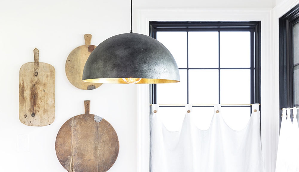 A black ceiling pendant next to a wall decorated with cutting boards