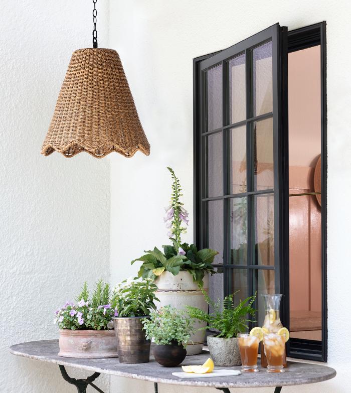 A natural brass sconce with a white shade on a dark wall colored wall next to a pot of flowers