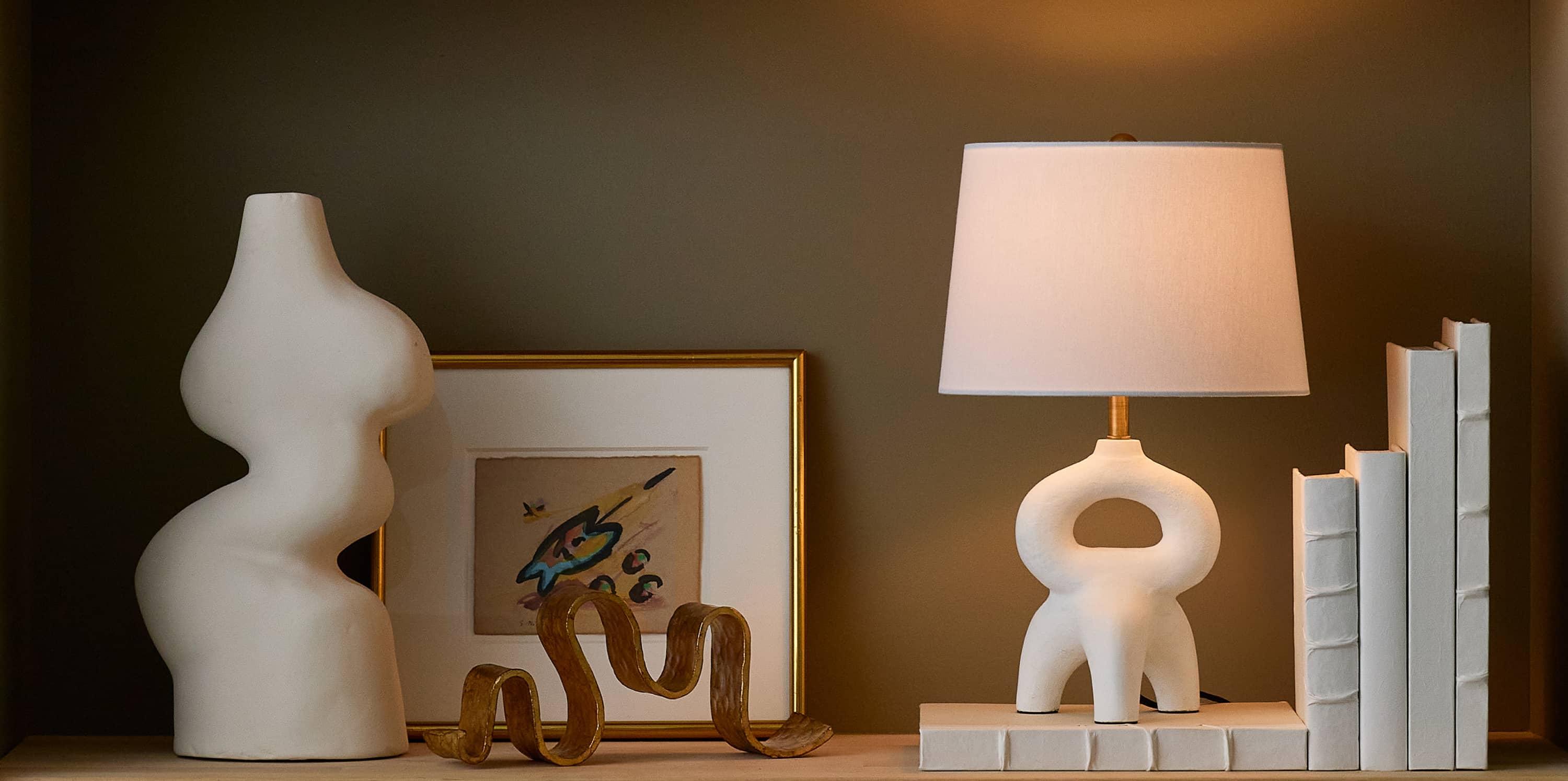 shelf with white books white mini table lamp and gold picture frame