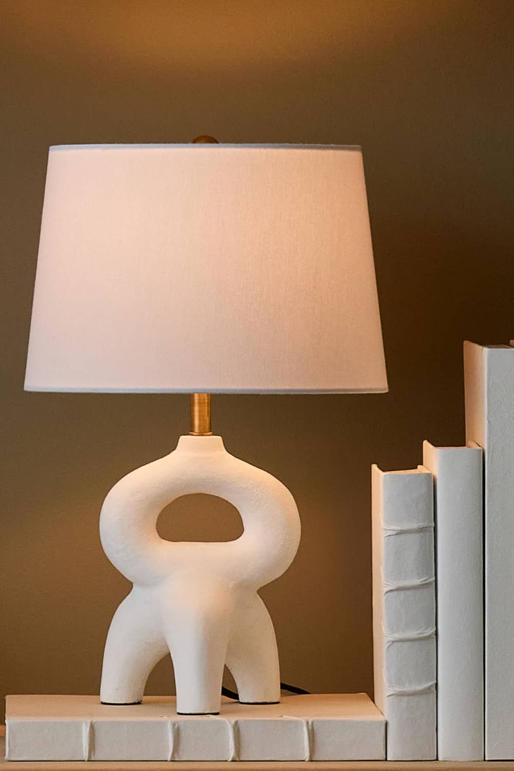 shelf with white books holding a white mini table lamp