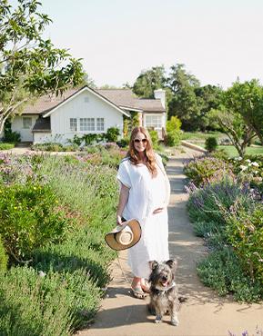 Kitchey Kitchen standing with her dog in front of a field of wild flowers and a home