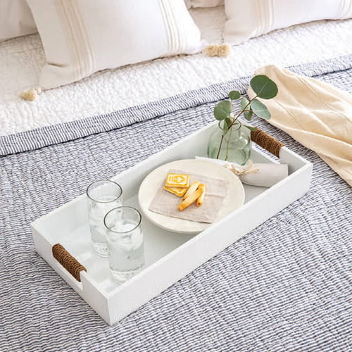 Coastal styled bed with a leather tray containing glasses of water and snacks