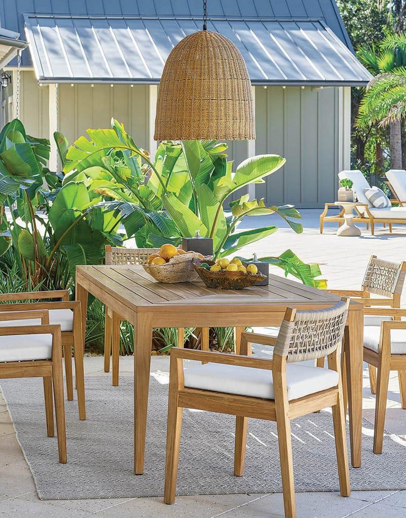 Coastal outdoor patio with a light wood table and chairs, and a woven rattan pendant light