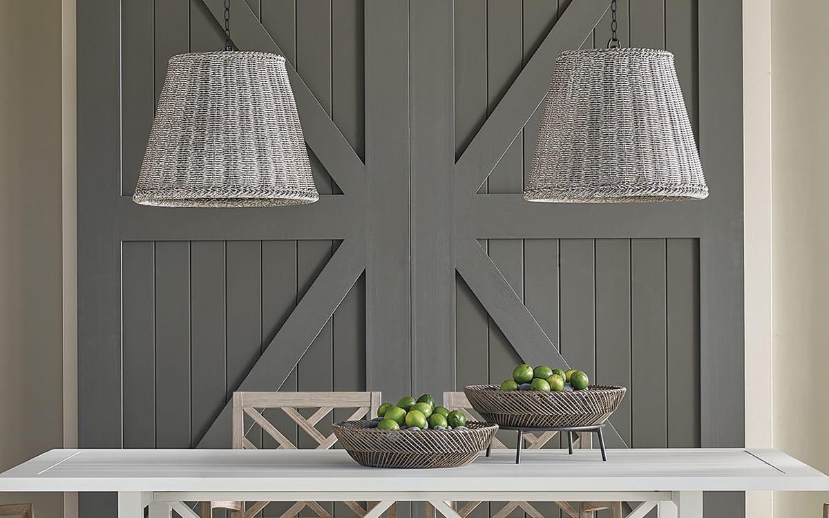 Coastal outdoor patio with gray barn doors, a white table, and two gray woven ratten pendant lights