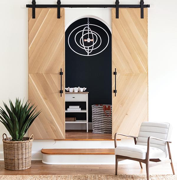 Living room with sliding barn doors, a white and natural wood chair, and a coastal inspired white circle chandelier