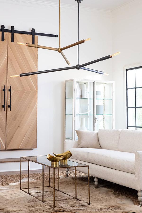 Livingroom with glass and metal coffee table, white couch, and two modern natural brass and oil rubbed bronze chandeliers