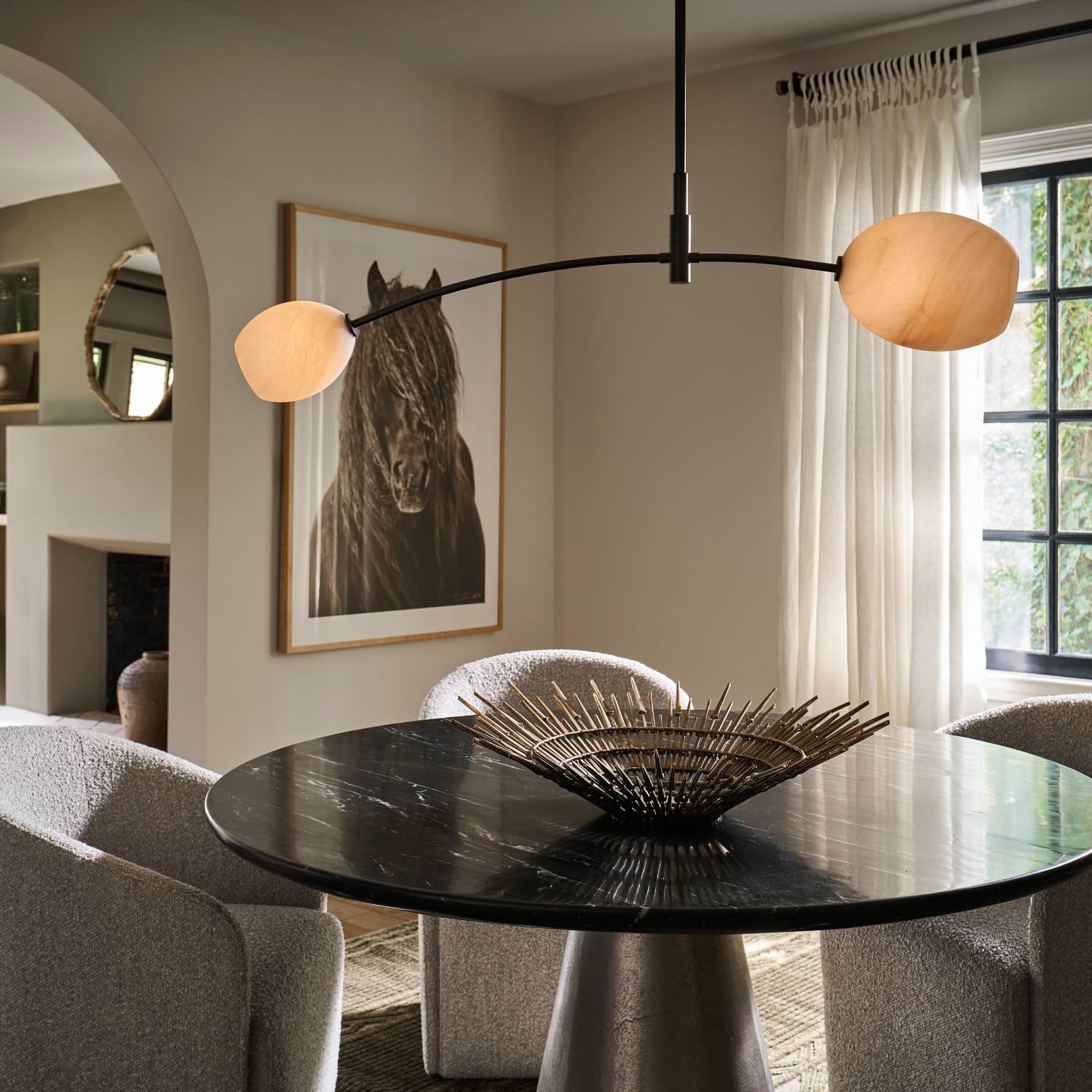 Dining room with circular table holding a bowl with a black and alabaster chandelier hung above it