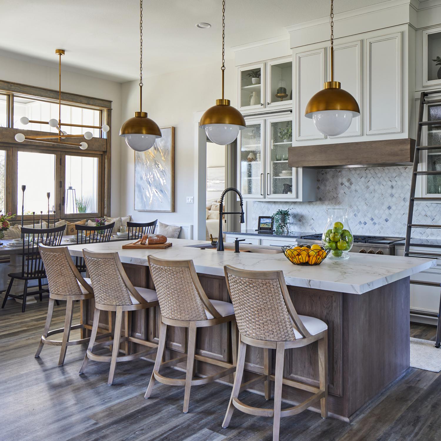 kitchen island with four chairs and three brass and glass pendants hanging above it