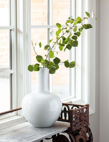Window with a wooden bench and white vase with leaves in it